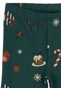 Katoenen legging met een donkergroene achtergrond, versierd met feestelijke patronen zoals cadeaus, sneeuwvlokken, zuurstokken en hulst.