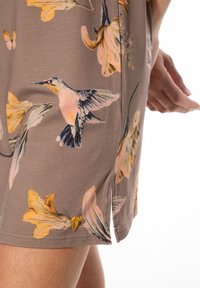 Brauner Stoff mit floralem Muster, gelben Blumen und einem Kolibri. Verfügt über einen seitlichen Schlitz und eine kleine gelbe Schleife als Akzent.