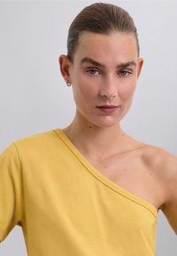 Haut jaune à une épaule en tissu lisse et léger. Doté d'un décolleté large et d'une coupe décontractée. Design simple et contemporain.