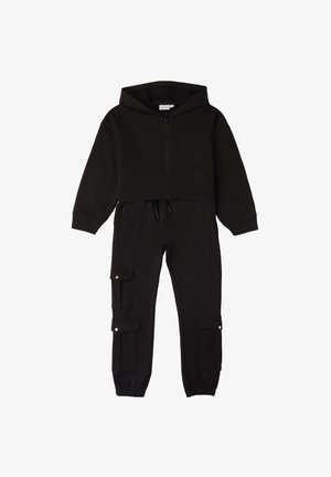 Felpa nera corta con zip frontale e coulisse; abbinata a pantaloni a sigaretta con tasche cargo e polsini elasticizzati.