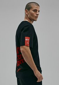 Czarna koszulka bawełniana z czerwoną grafiką na plecach i czerwoną metką na rękawie. Krótkie rękawy i standardowy krój.