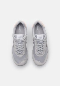 Gray athletic shoes featuring a mesh upper with suede accents, rounded toe, lace-up design, and a subtle peach detail on the heel.