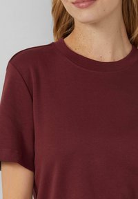 Camiseta de cuello redondo burdeos hecha de algodón suave, con mangas cortas y una textura lisa, con un diseño sencillo y sin logotipos visibles.