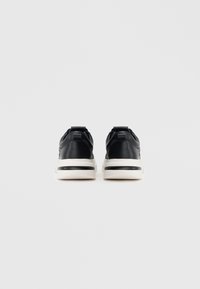 Mustad nahast tossud valge vahepealse tallaga, ümar kuju ja kontrastsete mustade detailidega. Kannatab asukoht mugavuse tagamiseks jalga panemisel.