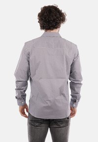 Camicia a maniche lunghe di colore blu con un motivo geometrico. Presenta un colletto classico e polsini con bottone. Il tessuto sembra leggero e ha una texture liscia.