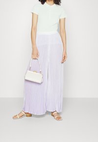 Vihreä pikeepaita napitusyksityiskohdalla, yhdistettynä purppuran- ja valkoviirullisiin leveälahkeisiin housuihin. Asusteena valkoinen käsilaukku ja sandaalit.