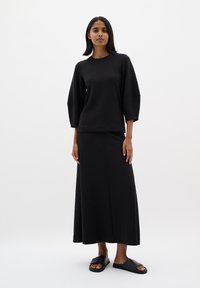 Sort sweatshirt med trekvartærmer, parret med en lang sort nederdel og sorte skridsikre sandaler. Glat stof med et afslappet design.