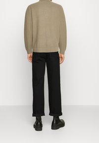 Maglione beige a maglia con texture a coste, abbinato a pantaloni neri con risvolto e stivali neri spessi, visti da dietro.