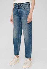 Jasnoniebieskie, wysokiej talii dżinsy o luźnym kroju, z pięcioma kieszeniami i wyraźnym śladami przetarcia. Połączone z jasnymi trampkami.