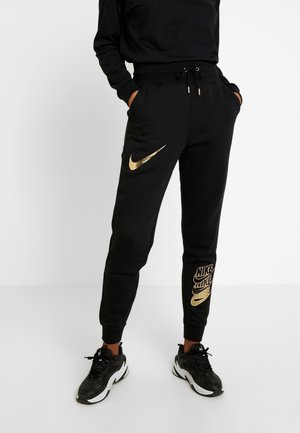 Czarne dresy z materiału bawełnianego, ozdobione metalicznym złotym logo Nike na udzie i wyraźnym brandingiem na dolnej części nogawki. Regularny krój.
