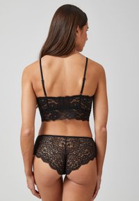 Bralette en dentelle noire avec bretelles ajustables et bords festonnés, associé à une culotte en dentelle assortie, mettant en avant un motif floral et une texture semi-transparente.