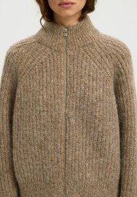 Cardigan en mélange de laine beige avec un col haut, un design côtelé texturé et une fermeture éclair argentée. Doux et chaud avec une coupe décontractée.