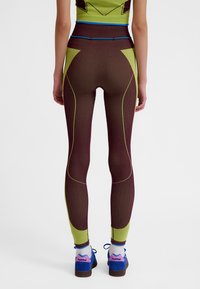 Tætsiddende leggings med en vinrød krop og limegrønne detaljer, der har en ribbet tekstur og kontrasterende blå syninger langs sømmene.