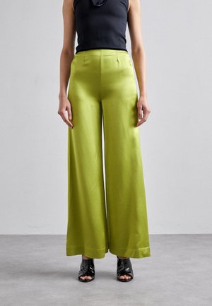 Wijduitlopende, felgroene broek van gladde, glanzende stof met een hoge taille, gecombineerd met zwarte open teenschoenen. Eenvoudig ontwerp met een schone afwerking.