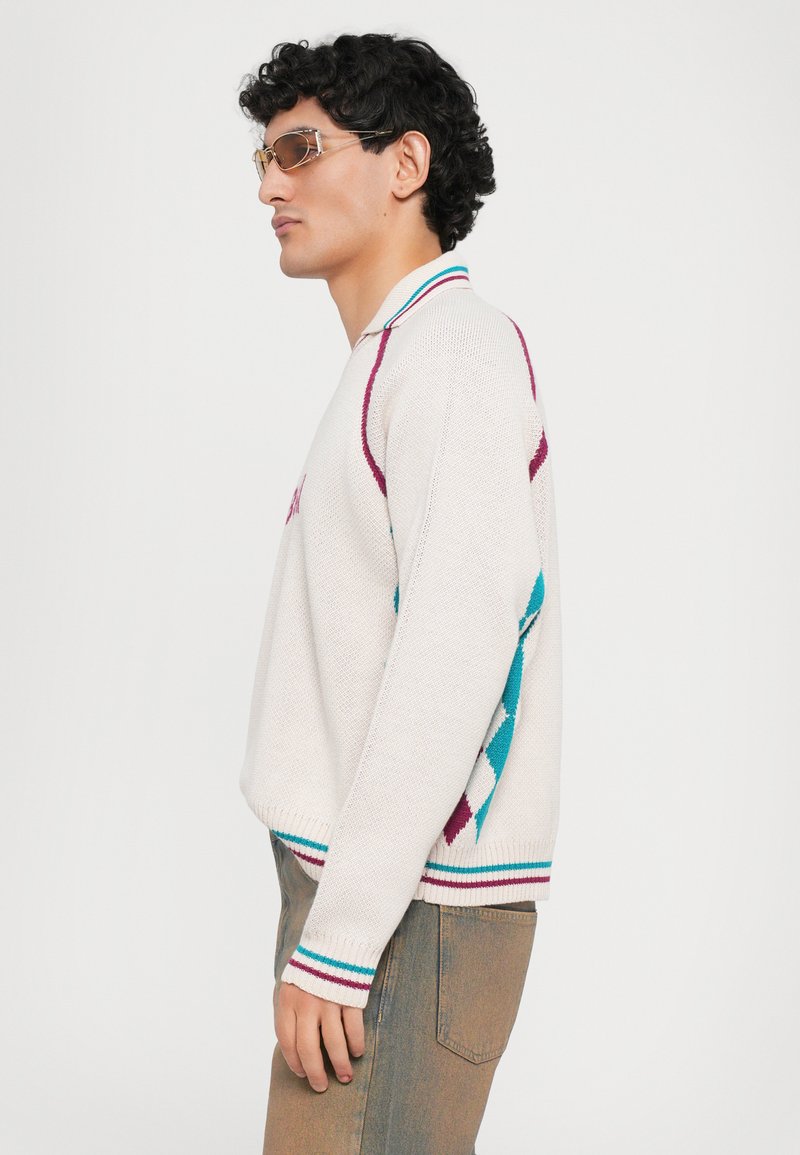Pull en tricot blanc texturé avec des motifs géométriques teal et bordeaux, avec des rayures contrastantes au col et aux poignets, et une coupe décontractée.