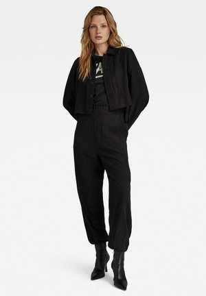 En sort cropped jakke med knaplukning, parret med løse sorte bukser. Sorte hælede ankelstøvler fuldender outfittet og skaber et monokromt look.