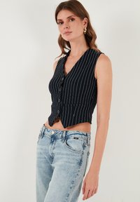 Námornícky modrý a biely pruhovaný skrátený top s výstrihom do V, zapínaním na gombíky a dvoma prednými vreckami, skombinovaný so svetlými deniminovými džínsami.