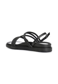 Sandalias negras con tiras cruzadas de material texturizado, suela plana y hebilla ajustable en el tobillo. Diseño minimalista.