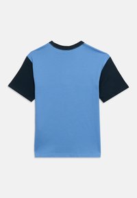 Κοντομάνικη μπλούζα με ανοιχτό μπλε σώμα, μαύρα μανίκια και μαύρο στρογγυλεμένο λαιμό, εμφανιζόμενη από πίσω σε λευκό φόντο.