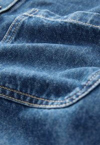 Denim w głębokim niebieskim kolorze, z widocznym szwem, miękką fakturą i subtelnymi różnicami w wzorze splotu.