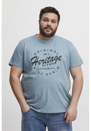 Svijetloplava pamučna majica s okruglim izrezom. Ima veliki crni grafički print koji kaže "Original No. 1 Heritage Blend Blue Denim."
