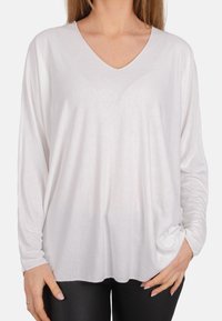 Weißes Langarmshirt mit V-Ausschnitt, lässiger Passform und weicher Textur. Der Stoff liegt locker am Körper an und hat seitliche Raffungen.