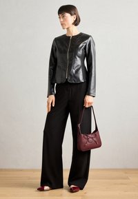 Black leather jacket with a zip front, paired with wide black trousers, and a maroon handbag featuring a bow detail. Silver accent on shoes.