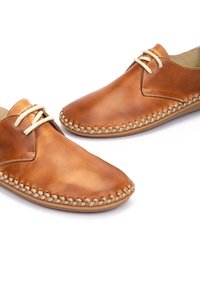 Zapatos de cuero marrón con una textura suave, punteras redondeadas y costuras decorativas a lo largo de los bordes. Presentan cordones de color claro.