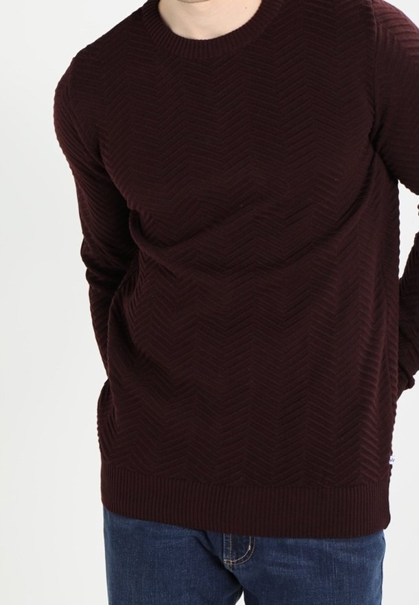Burgundy texturerad tröja med fiskbensmönster, rund hals, och ribbade ärmslut och fåll. I kombination med blå jeans.