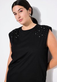 Schwarzes T-Shirt mit kurzen Ärmeln und Verzierungen an den Schultern. Aus glattem Stoff gefertigt, mit Rundhalsausschnitt und lässiger Passform.
