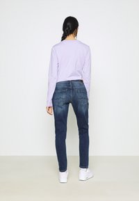 Top a maniche lunghe color lavanda abbinato a jeans in denim blu scuro. Presenta una vestibilità aderente, un design classico a cinque tasche e cuciture sottili sulle tasche.