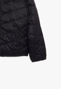 Zwarte gewatteerde jas met een mouw en zijkant met horizontale stiksels en een schuine zak zichtbaar op een witte achtergrond.