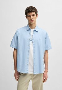 Camicia azzurra a maniche corte con colletto button-down, caratterizzata da una leggera texture e un piccolo logo sul lato sinistro.