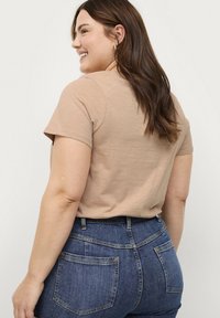T-shirt beige a maniche corte con una consistenza morbida, vestibilità rilassata e scollatura tonda. Abbinato a jeans in denim blu a vita alta con tasche posteriori.