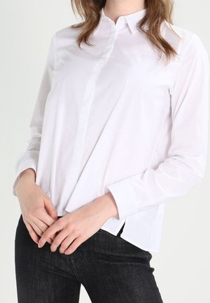 Wit overhemd met lange mouwen en een kraag, voorzien van een knoopsluiting aan de voorkant, een gladde textuur en een getailleerde pasvorm. Gecombineerd met een donkere spijkerbroek.