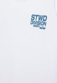 Tissu blanc avec un texte bleu "STWD DIVISION 1991" et un logo géométrique bleu en dessous, sur le côté supérieur gauche.