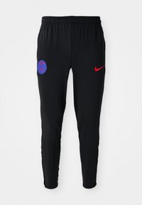 Black athletic pants made from smooth fabric. Features red Nike logo and blue Paris emblem on the left. Elastic waistband with tapered legs.