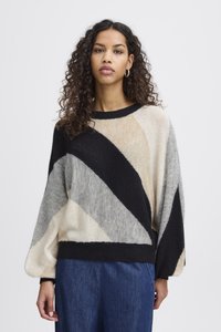 Pull en tricot avec un motif diagonal en noir, beige, gris et crème. Coupe ample avec un col côtelé et des manches longues.