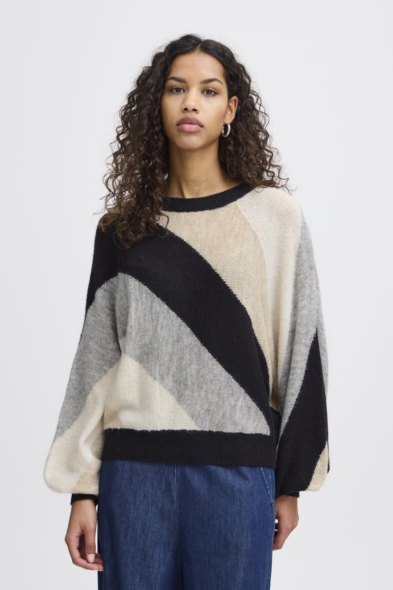 Pull en tricot avec un motif diagonal en noir, beige, gris et crème. Coupe ample avec un col côtelé et des manches longues.