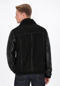 Veste noire avec un col en shearling, des manches en cuir avec une texture matelassée, des accents de boucles réglables et un corps lisse.