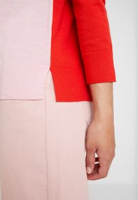 Sweter dziany z podziałem na czerwone i jasno-różowe sekcje, uzupełniony różowym teksturowanym materiałem poniżej. Dopasowane rękawy i dół.