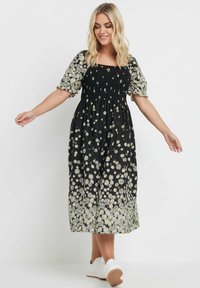 Svart blommig klänning med korta puffärmar, smockad bodice och vitt tusensköna mönster som bleknar vid fållen. Matchad med vita sneakers.