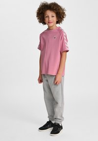Lyserød bomulds t-shirt med korte ærmer og hvide chevron-striber. Matchet med grå sweatpants og sorte sneakers, med et enkelt design.