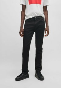 Jeans en denim noir avec une coupe slim, dotés de cinq poches et d'une taille classique. Associés à un t-shirt blanc avec un design graphique rouge.