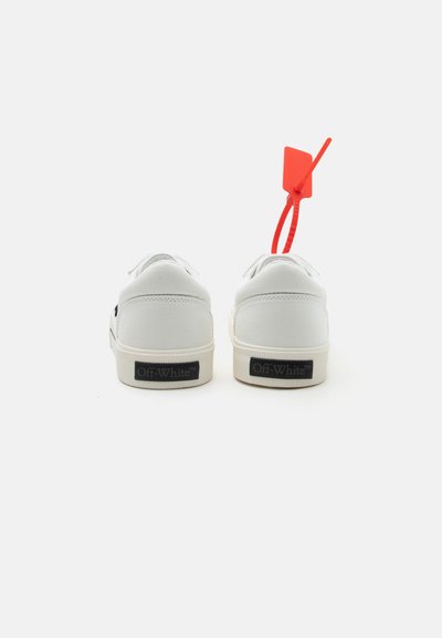 Ζευγάρι λευκών αθλητικών παπουτσιών Off-White, εμφανιζόμενα από πίσω, με μια κόκκινη πλαστική ετικέτα προσαρτημένη στο δεξί παπούτσι.