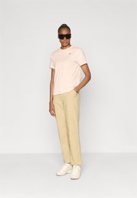 Lyserød bomulds t-shirt med korte ærmer og et lille blåt logo, parret med beige bukser og beige sneakers.