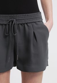 Grijze korte broek gemaakt van zachte stof met een elastische tailleband, trekkoord en zijzakken. Heeft lichte plooien voor extra ontwerpdetail.