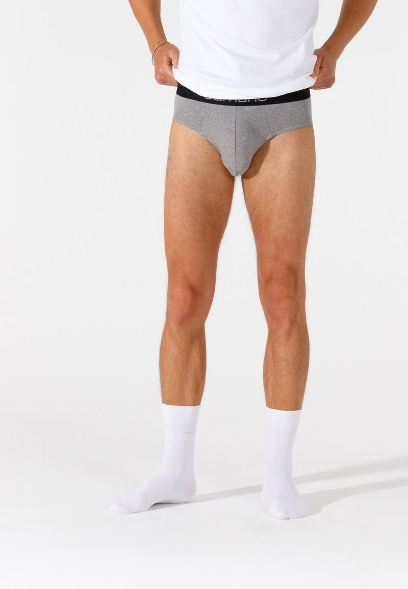 Slip di cotone grigi con un elastico nero in vita, indossati da una persona con calzini bianchi. Il tessuto ha una texture liscia.