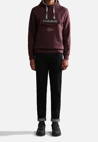 Sudadera con capucha burdeos, con cordones grises y parche de logo, combinada con pantalones negros y zapatillas negras con los puños enrollados.