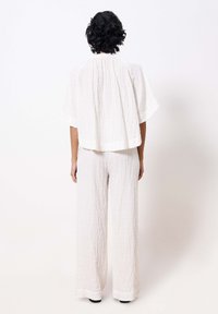 Witte, gestructureerde stoffen outfit met een losse top en brede broekspijpen. Achteraan is de plooidetail en vloeiende silhouet zichtbaar.